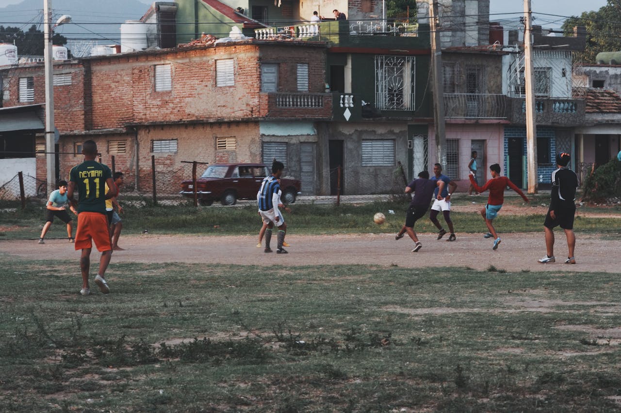 Group of young men playing football on an outdoor field in an urban neighborhood, showcasing community and sports.